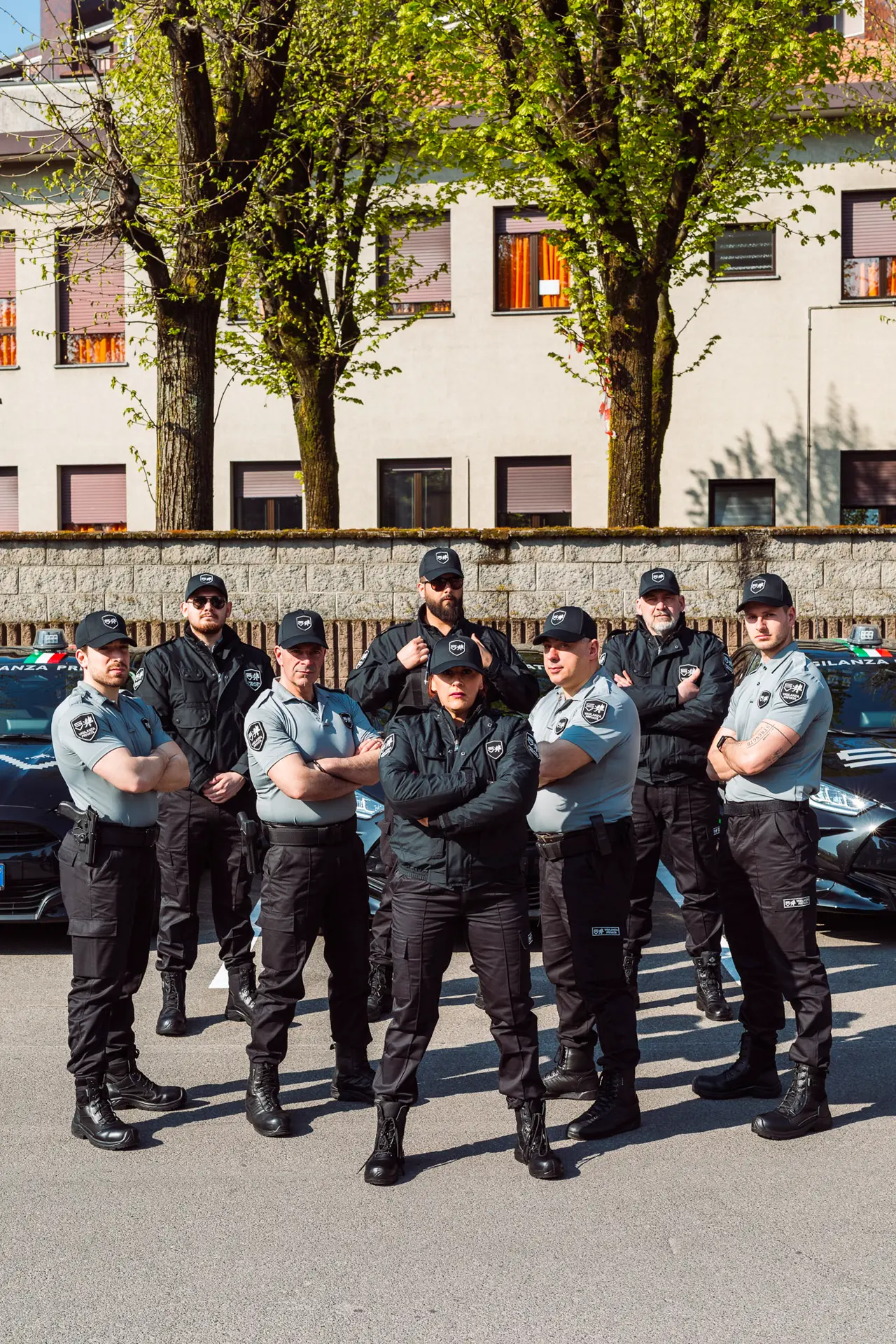Team di guardie giurate in divisa si dispone in formazione compatta e fiera all’esterno della sede aziendale, con le auto di servizio sullo sfondo. Lo scatto trasmette coesione, forza, spirito di squadra e affidabilità operativa del gruppo.