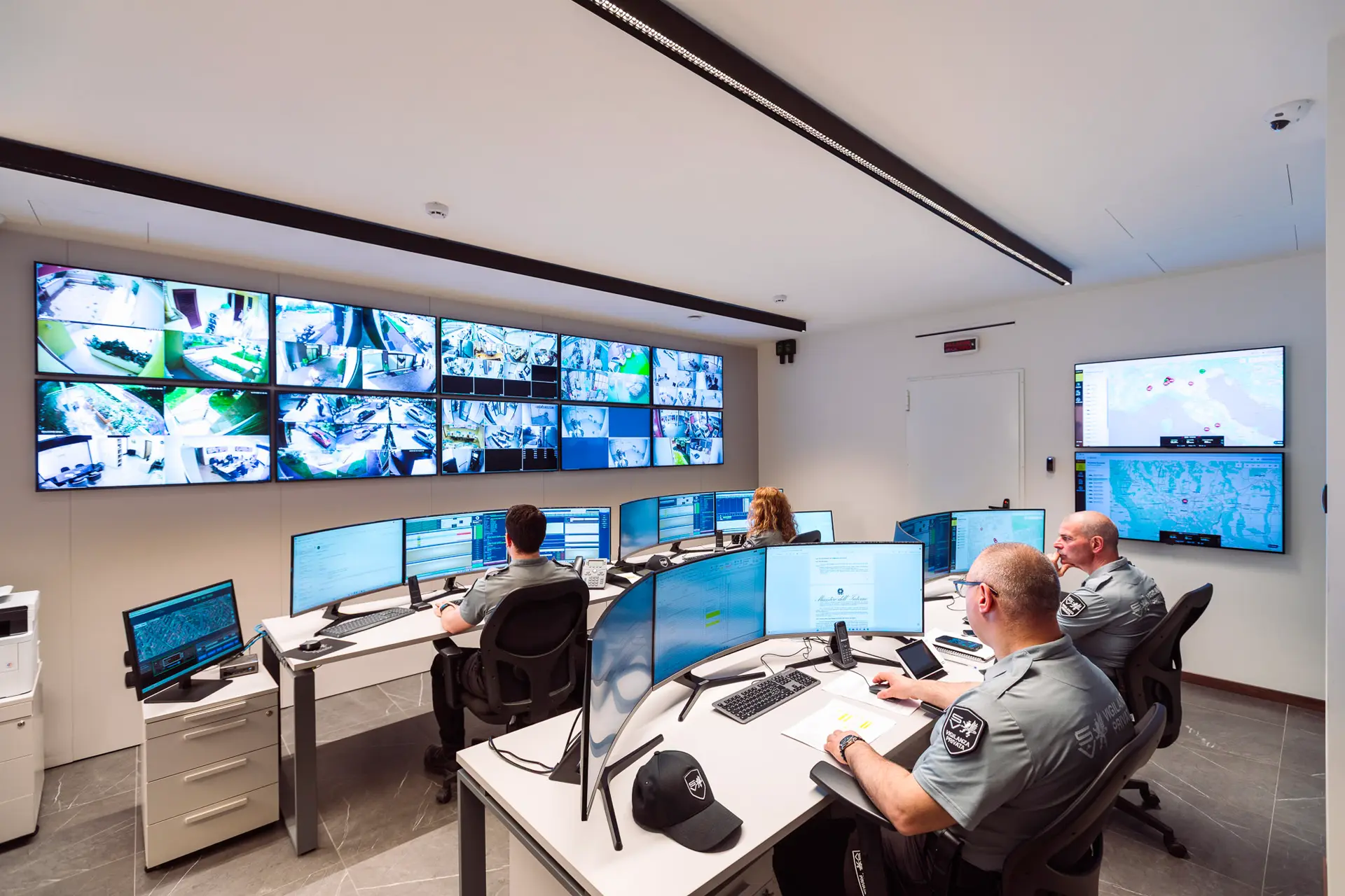 Sala controllo con operatori di vigilanza che monitorano decine di schermi di videosorveglianza in tempo reale.