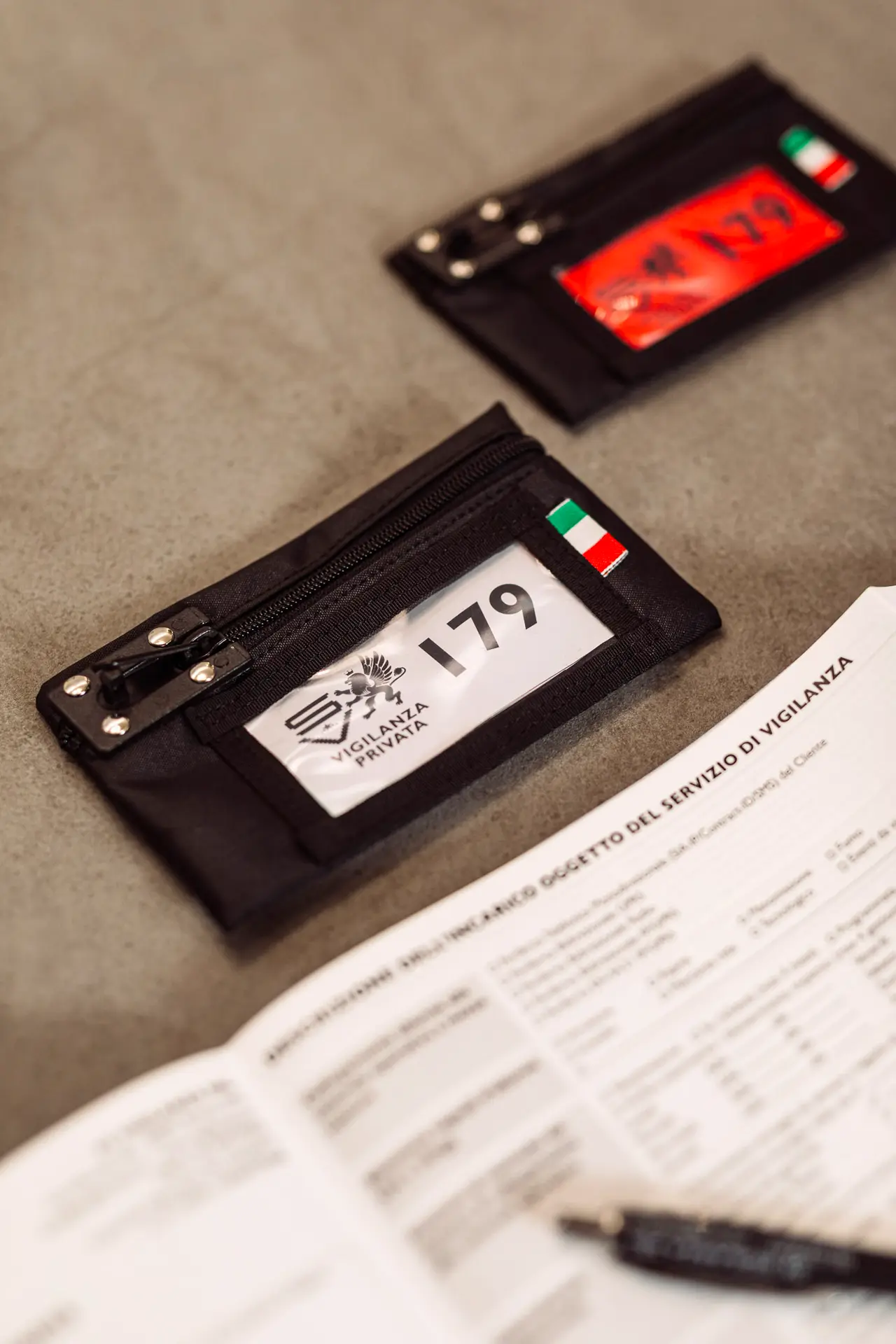 Bustina nera con etichetta numerata e bandiera italiana, accanto a un modulo stampato su un tavolo grigio.