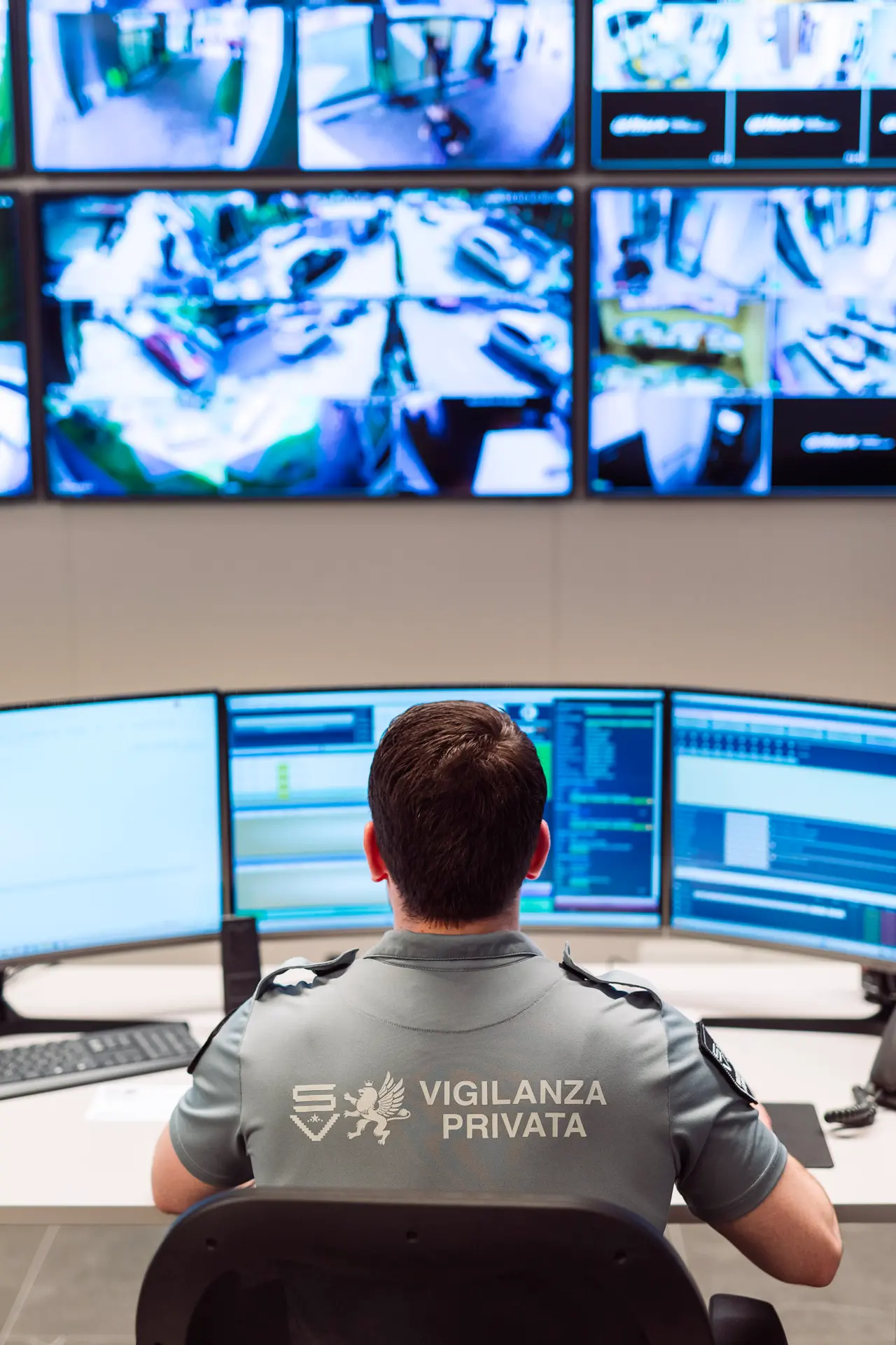 Agenti in divisa gestiscono sistemi di sorveglianza da postazioni con monitor multipli e linee telefoniche operative.